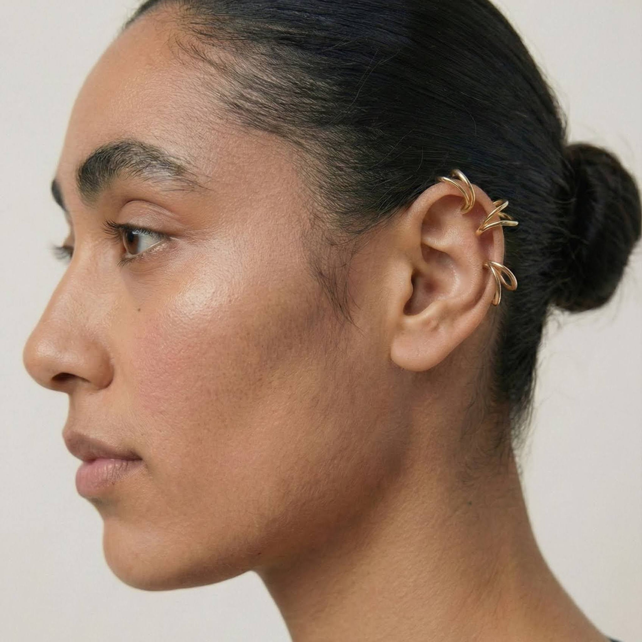 Close-up of a person wearing gold ear cuffs against a neutral background