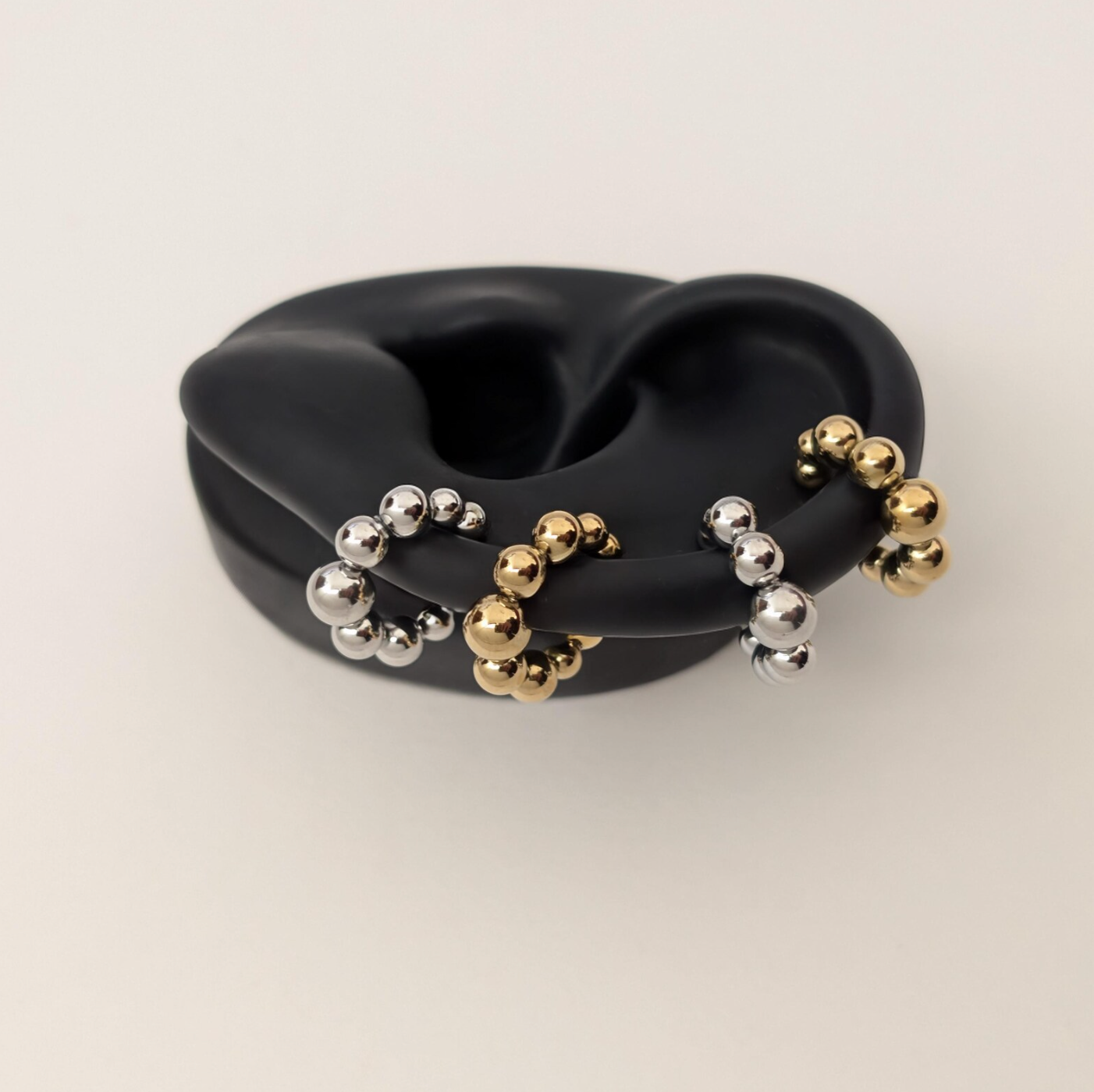 Ear cuff with gold and silver beads on a black silicone ear on light gray background