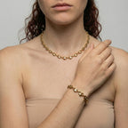 Woman wearing a gold chain necklace and bracelet against a neutral background
