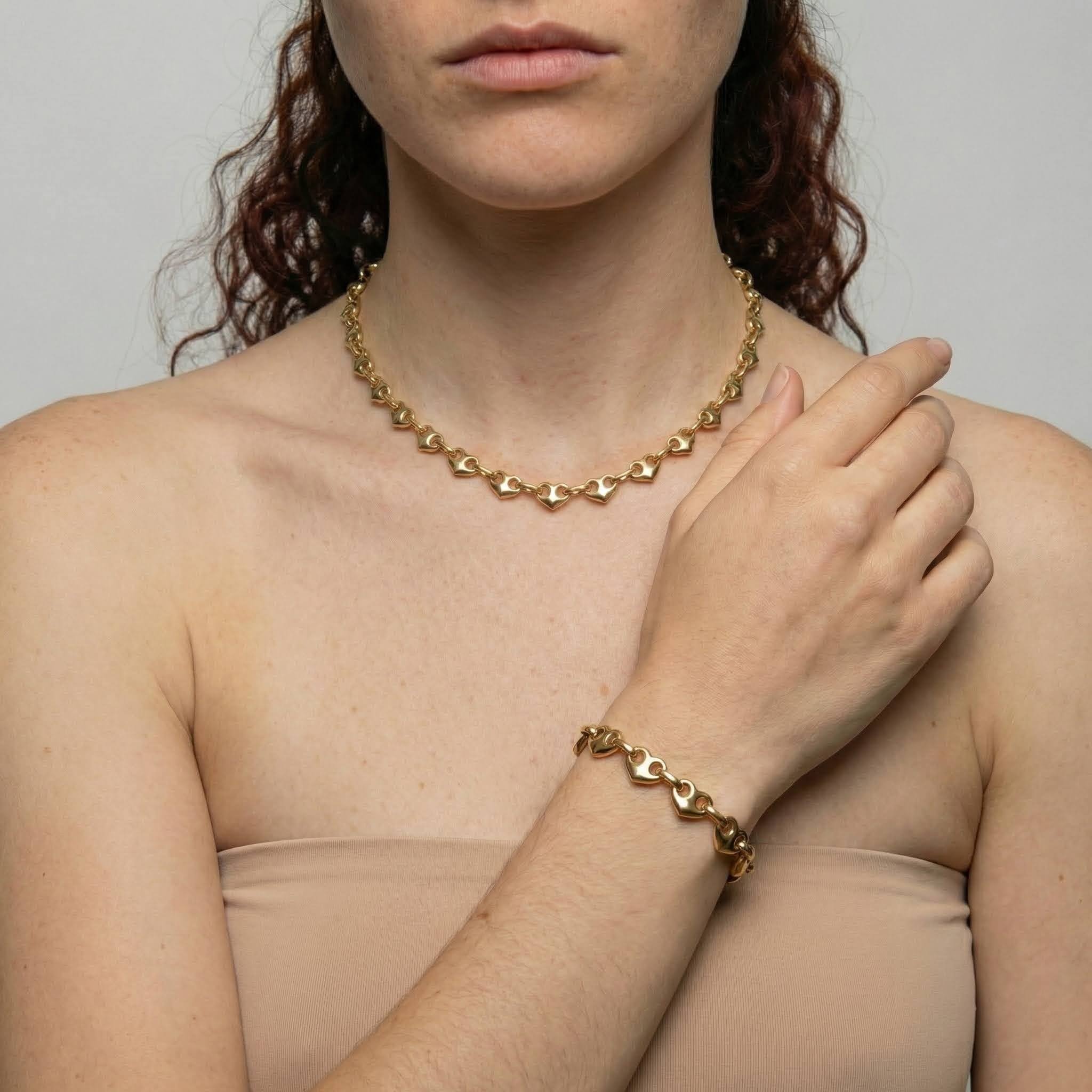 Woman wearing a gold chain necklace and bracelet against a neutral background