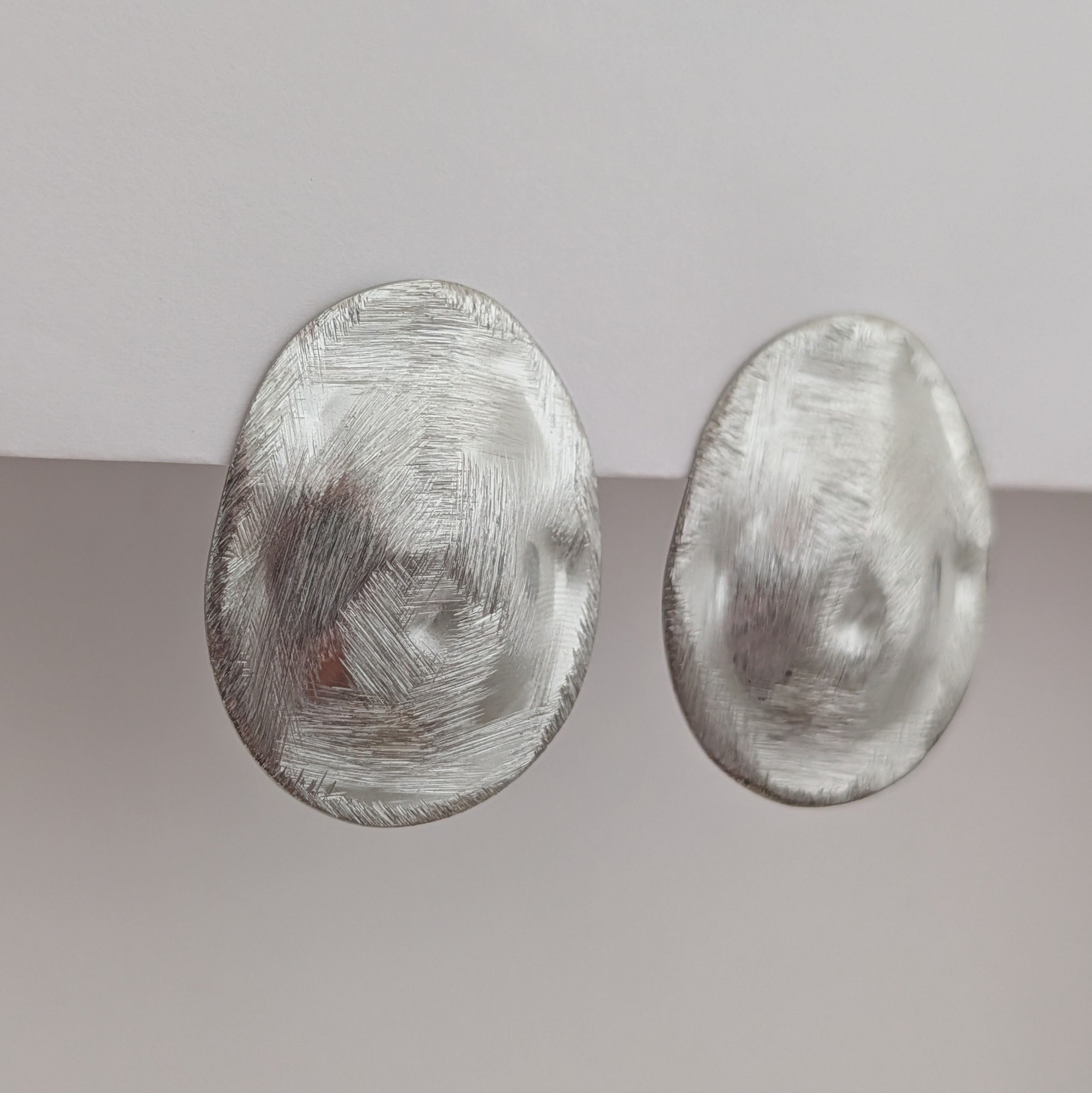 Pair of silver oval earrings on a gradient gray background