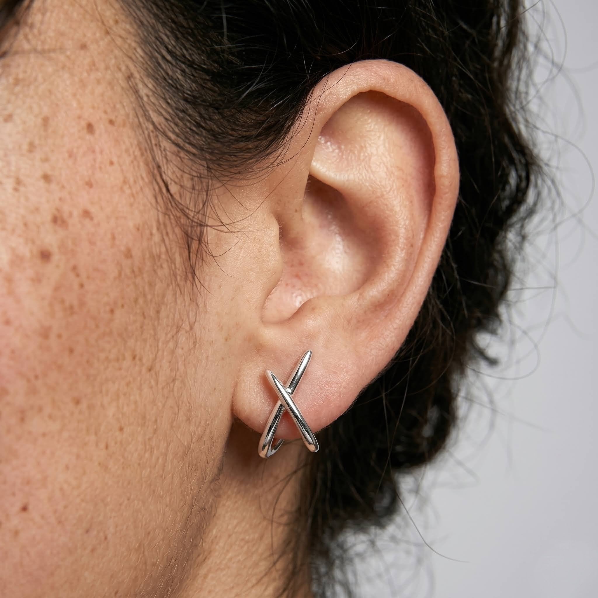 Close-up of an ear wearing a silver earring with a plain background