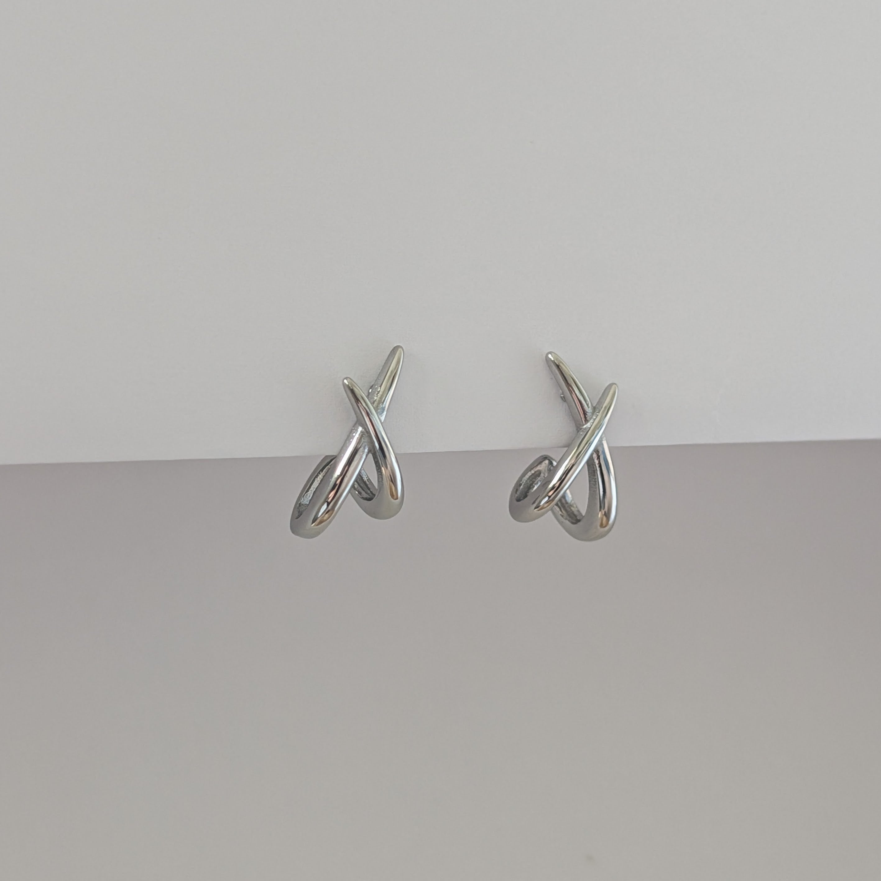 Pair of silver earrings on a gray surface with a light gray background