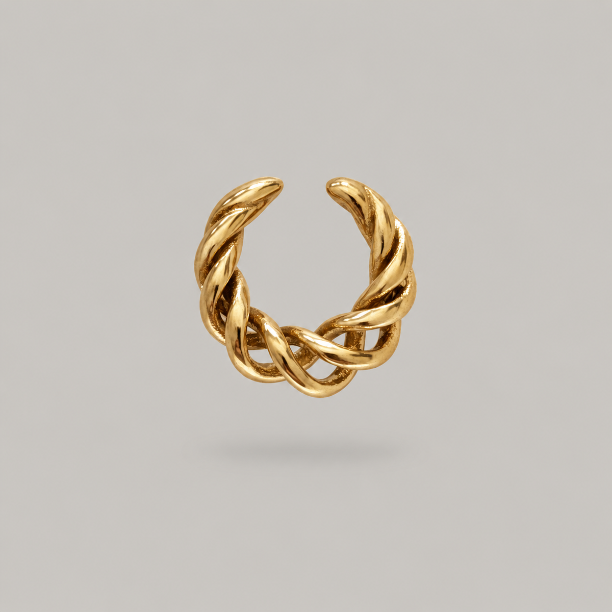 A gold twisted open ear cuff, no piercing ear wrap shown on a neutral light gray background.