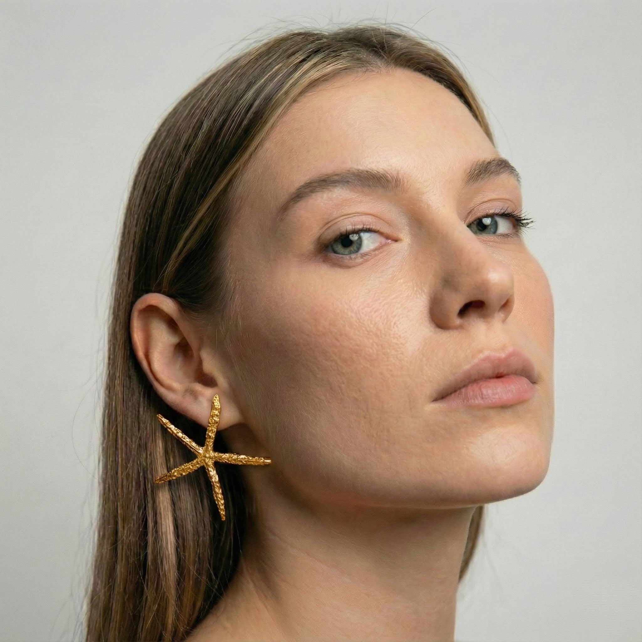 Woman wearing a gold starfish earring against a neutral background