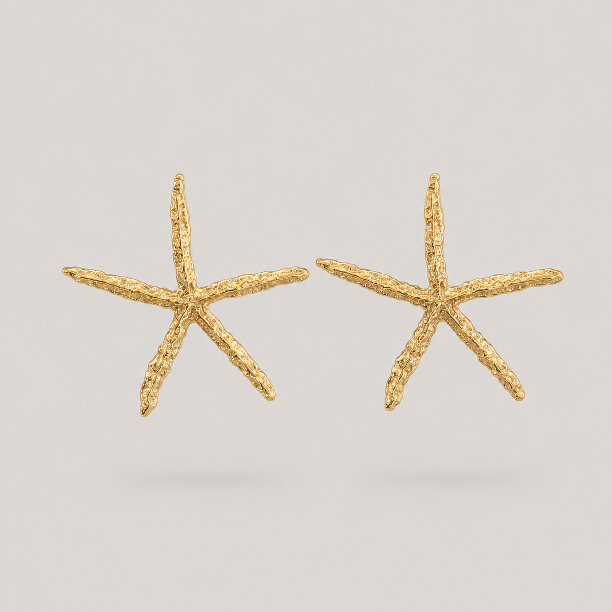 Gold starfish-shaped earrings on a light gray background