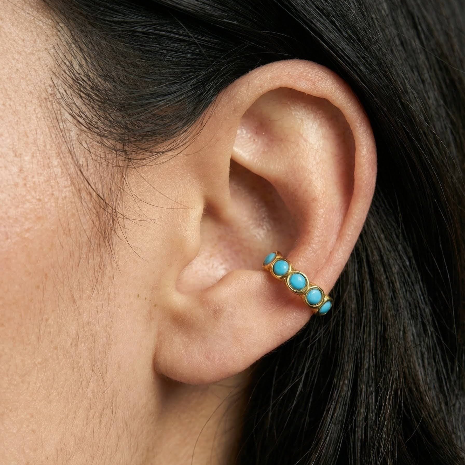 Close-up of an ear wearing a gold earring with turquoise stones