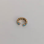 Gold ear cuff with blue stones on a light gray background