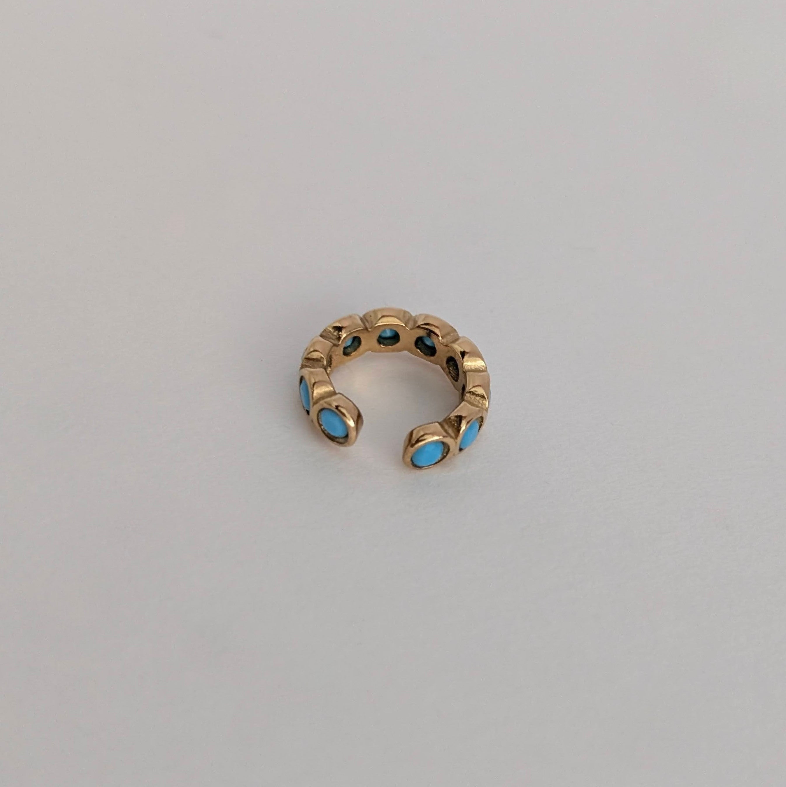 Gold ear cuff with blue stones on a light gray background