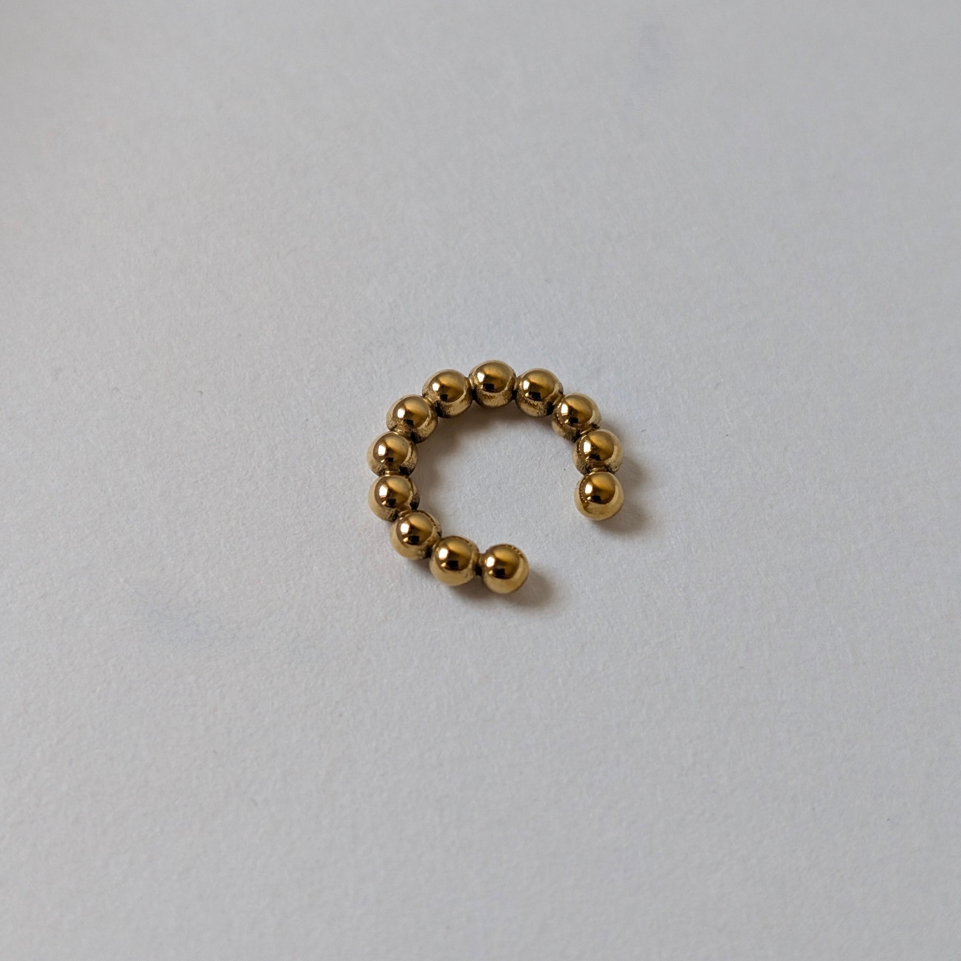 Flat‑lay of Fitta Mini gold ear cuff, waterproof and tarnish‑resistant, on white backdrop.