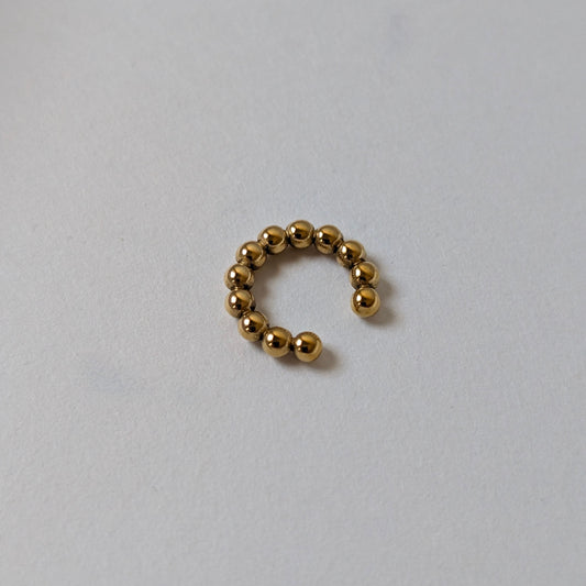 Flat‑lay of Fitta Mini gold ear cuff, waterproof and tarnish‑resistant, on white backdrop.