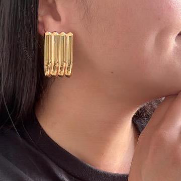On‑ear close‑up of gold chunky rectangle earrings, bold vintage look with hair up.