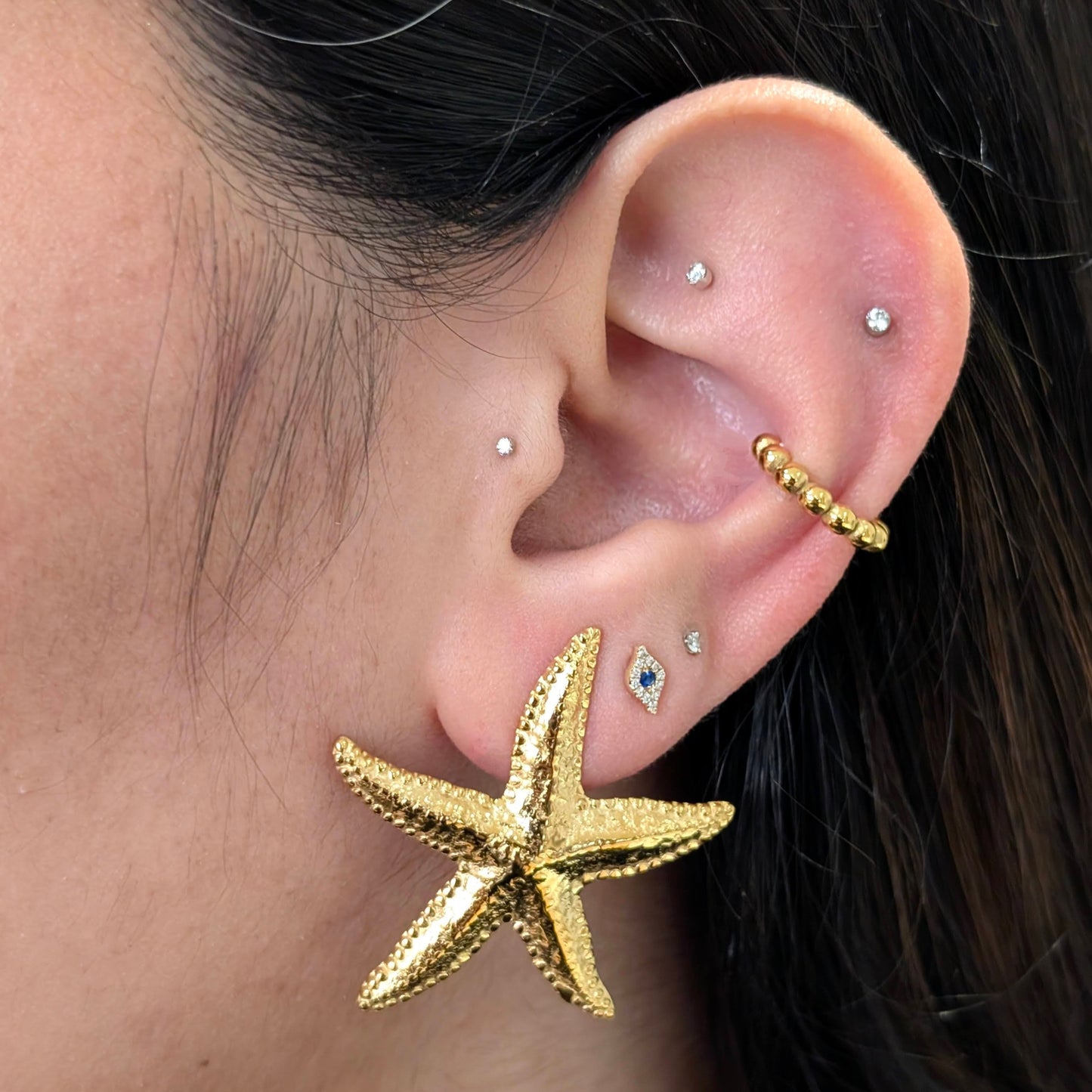 Layered gold ear stack featuring starfish stud earrings, beaded cuff and crystal studs—Étoile collection.