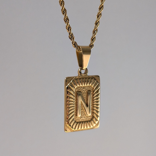 Macro close‑up highlighting engraved initial and polished 18k gold‑plated finish on medallion necklace.