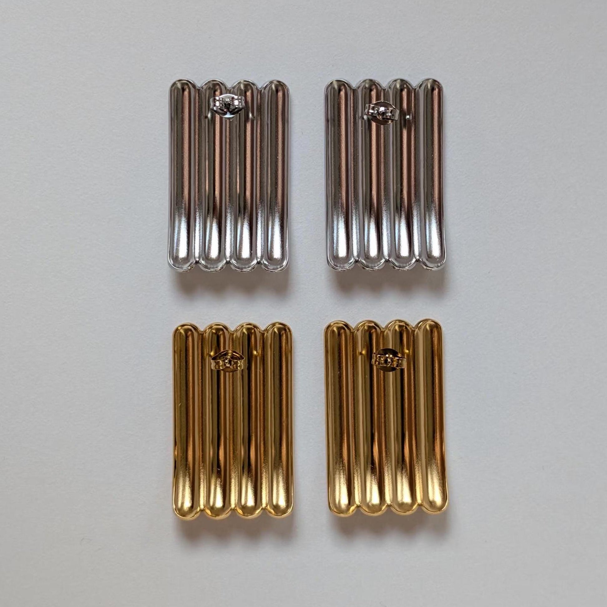 Reverse‑side comparison of gold and silver sculptural stud earrings, showing polished backs and stainless‑steel butterfly clasps.