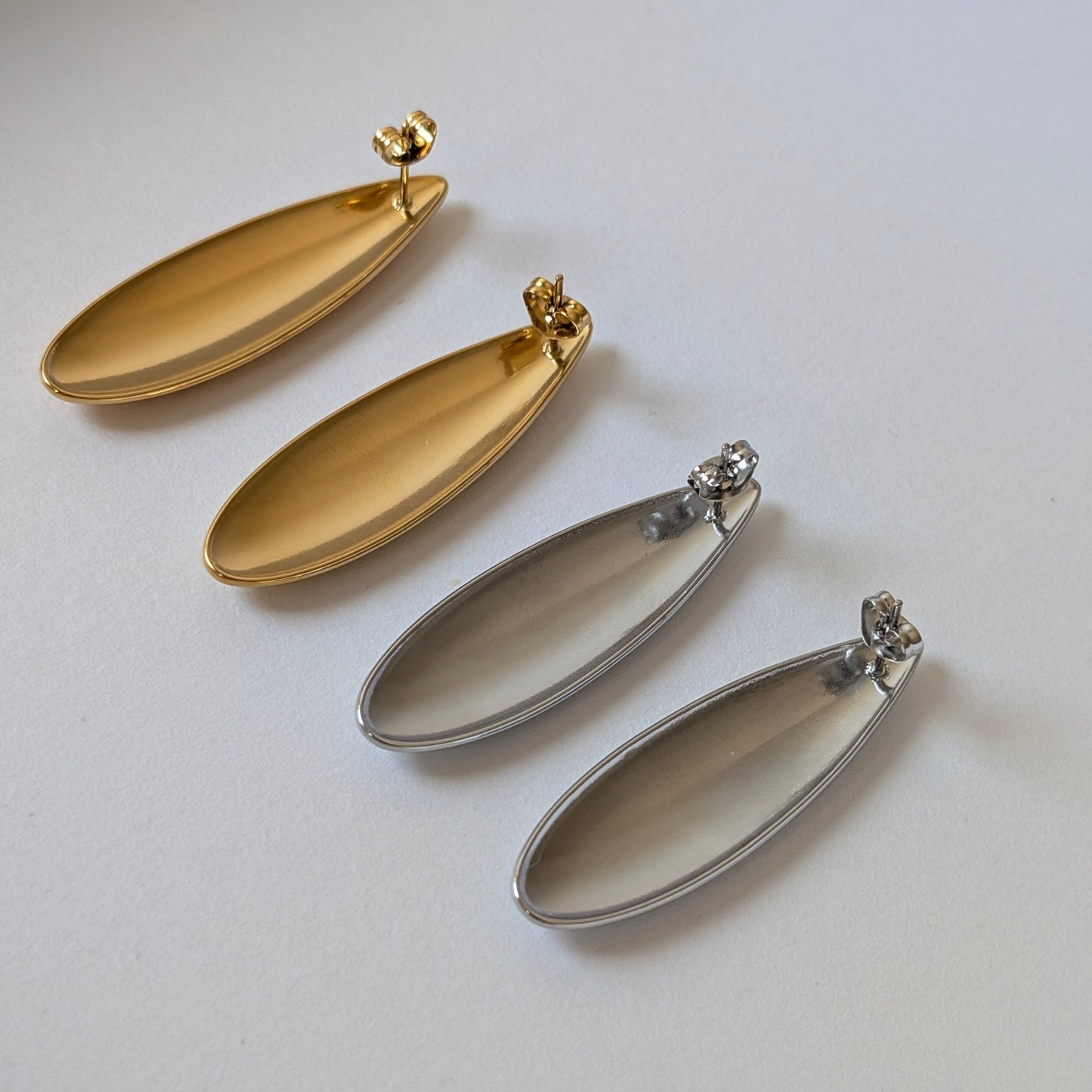 Back flat‑lay of gold and silver teardrop statement earrings with hypoallergenic steel posts and butterfly clasps.