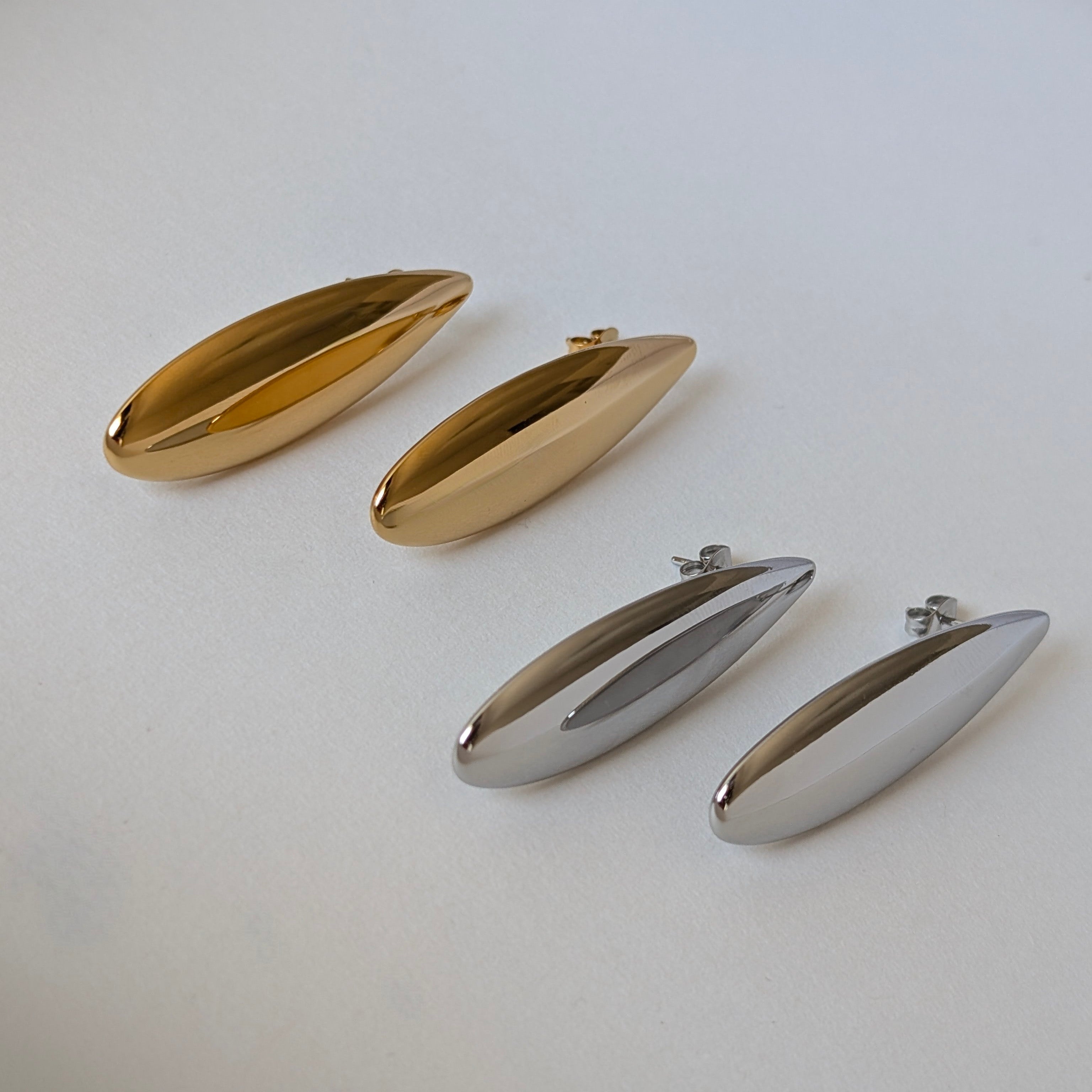 Profile view comparing gold and silver Raya teardrop statement earrings—slim drop silhouette, 4.53 cm length.