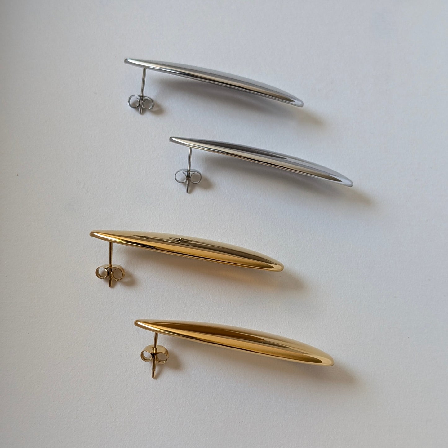 Side‑angle comparison of gold and silver teardrop statement earrings—Raya collection, 4.53 cm drop, high‑shine finish.