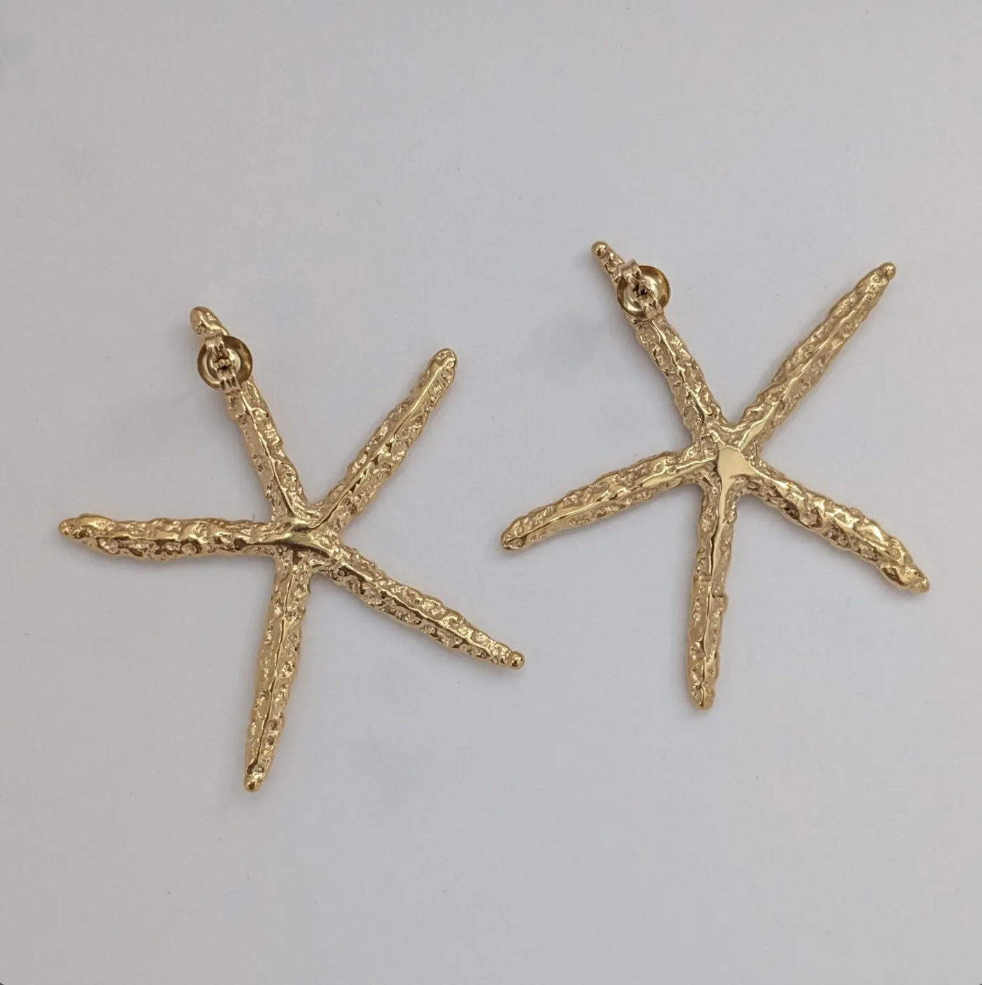Flat‑lay of waterproof, hypoallergenic gold starfish statement earrings on white backdrop.