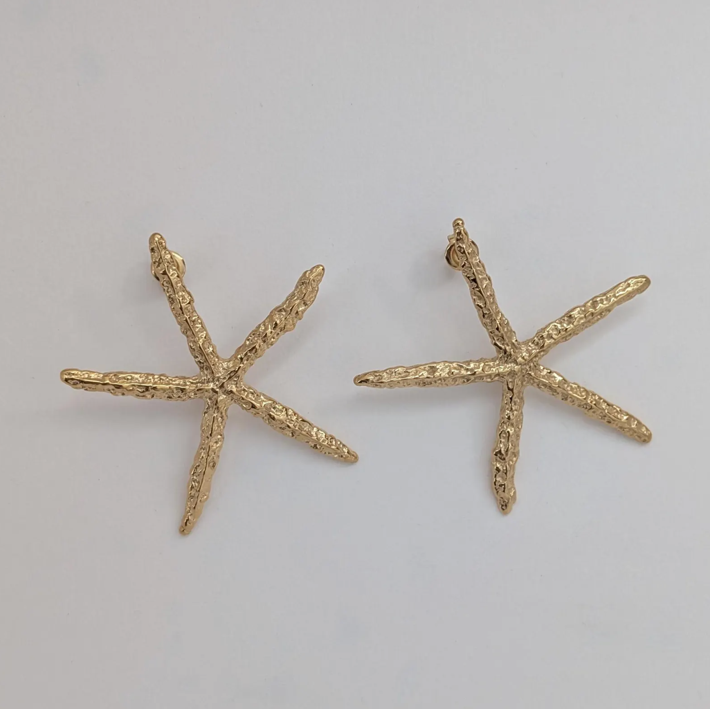 Flat‑lay of waterproof, hypoallergenic gold starfish statement earrings on white backdrop.