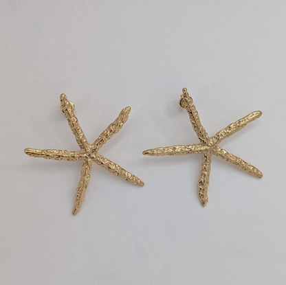 Flat‑lay of waterproof, hypoallergenic gold starfish statement earrings on white backdrop.