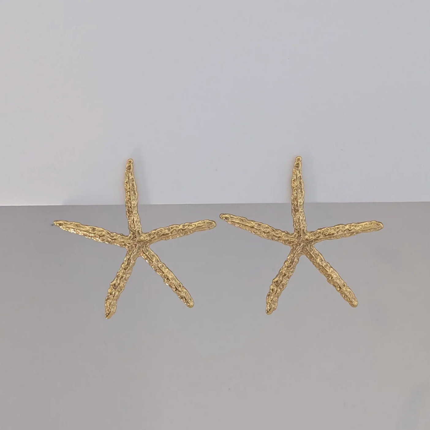 Front view of oversized gold starfish statement earrings—18k plated, polished texture.