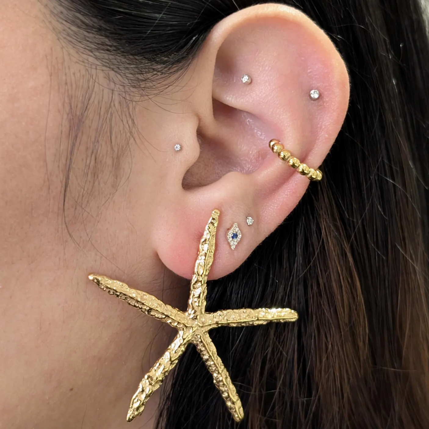 Lifestyle image of gold starfish statement earrings worn on ear—bold resort jewelry.