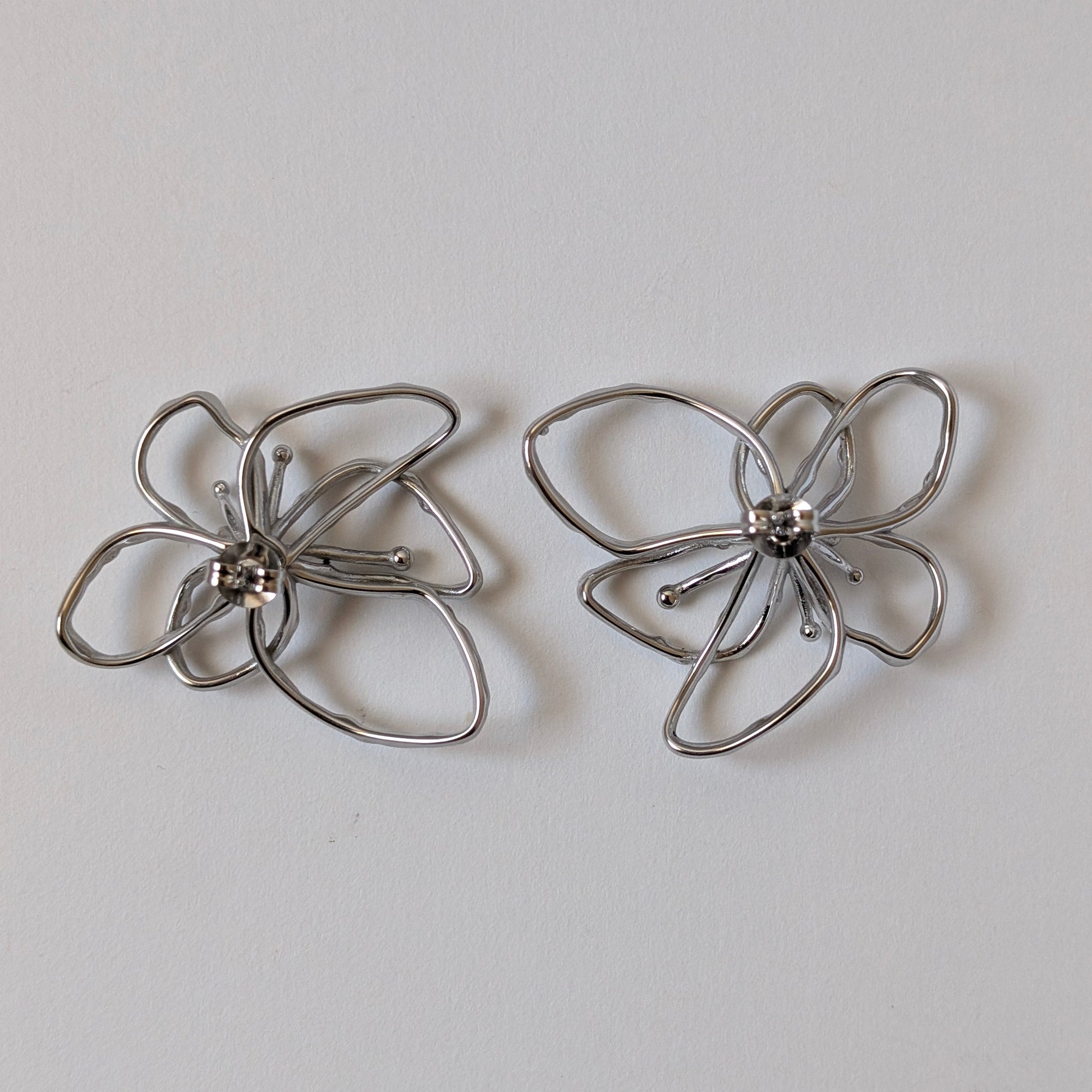 Flat‑lay of silver orchid statement earrings front side up, posts facing down on white backdrop—316 L steel petals.