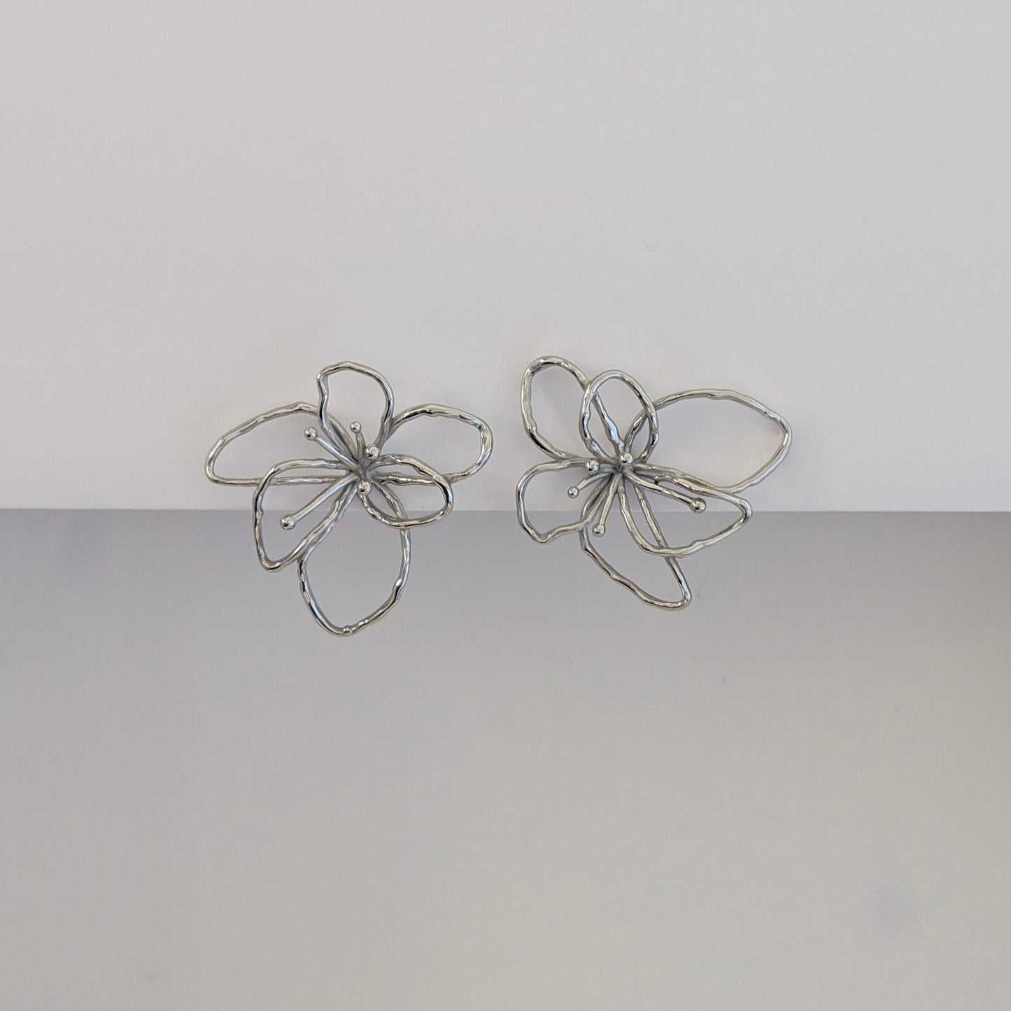 Front view of silver orchid statement earrings—polished stainless steel, sculptural petals, 4 × 4.21 cm studs.