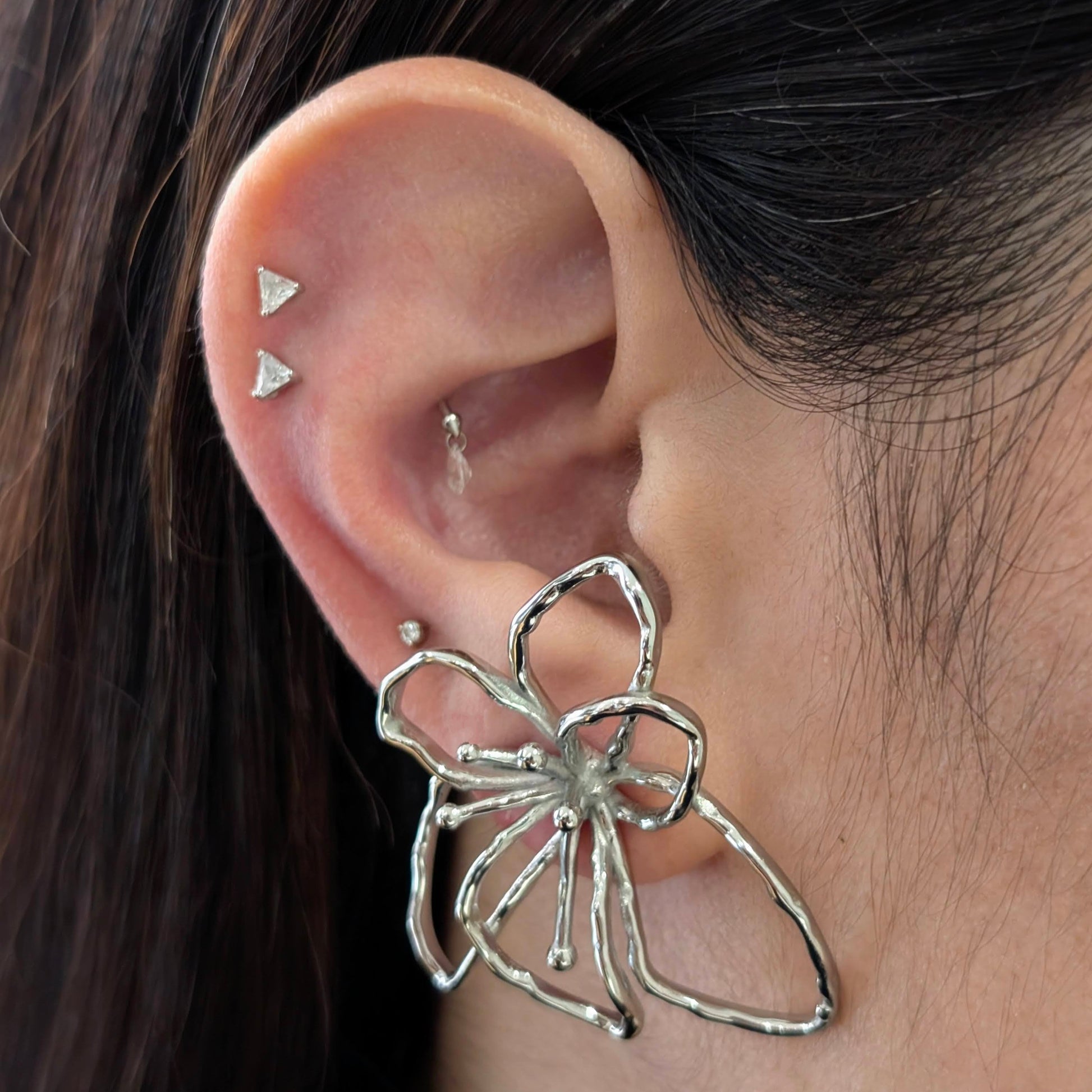 On‑ear close‑up of silver orchid statement earrings—polished stainless‑steel floral studs, 4 cm size.