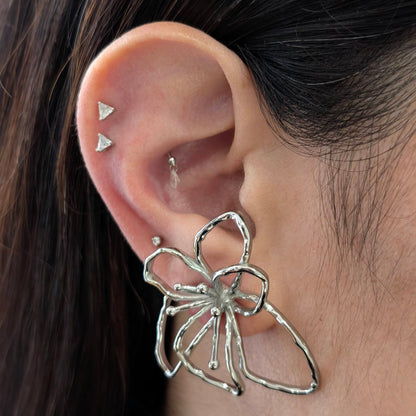 On‑ear close‑up of silver orchid statement earrings—polished stainless‑steel floral studs, 4 cm size.