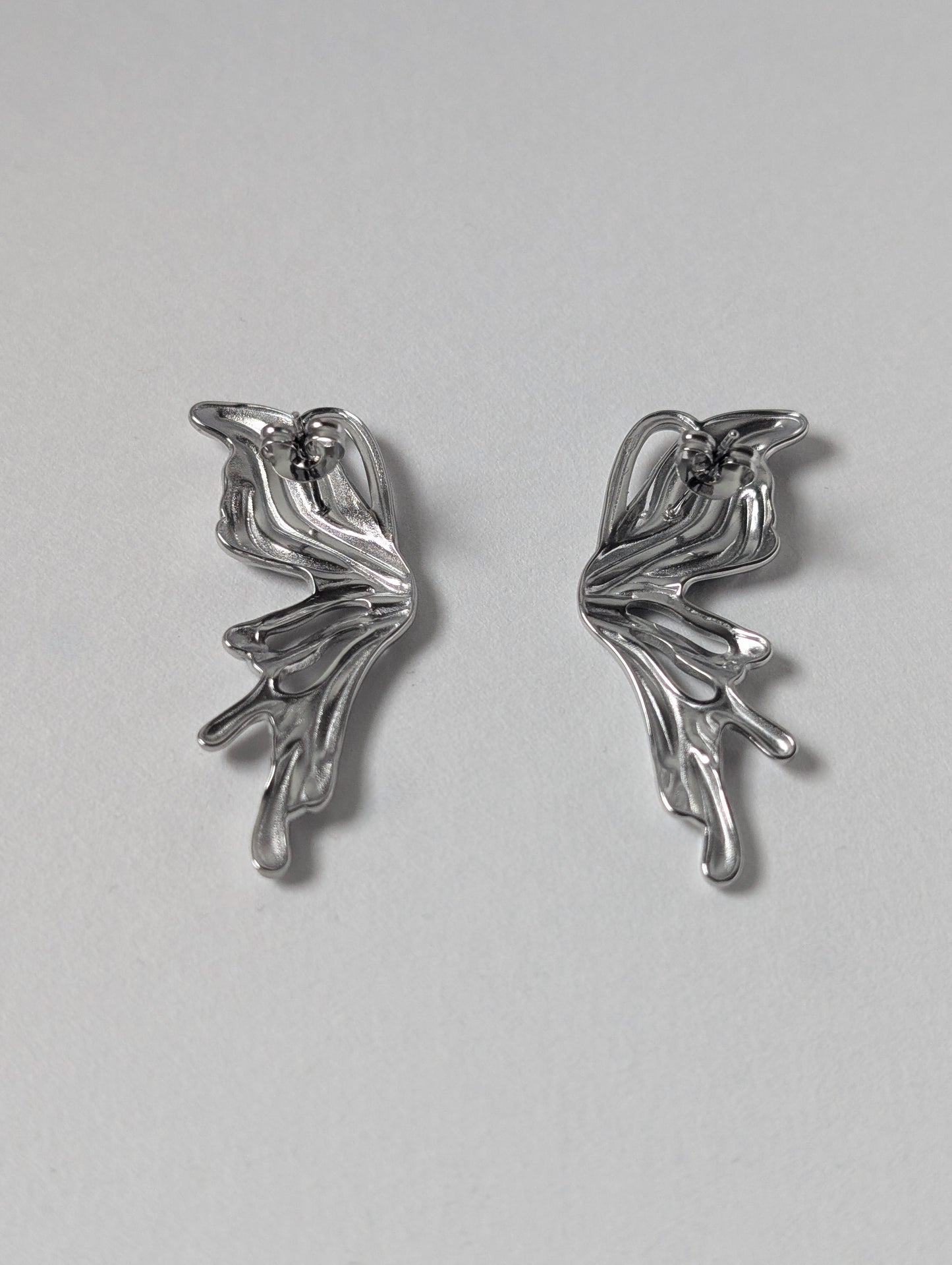 Back view of silver sculptural statement earrings showing stainless‑steel posts and secure butterfly clasp.