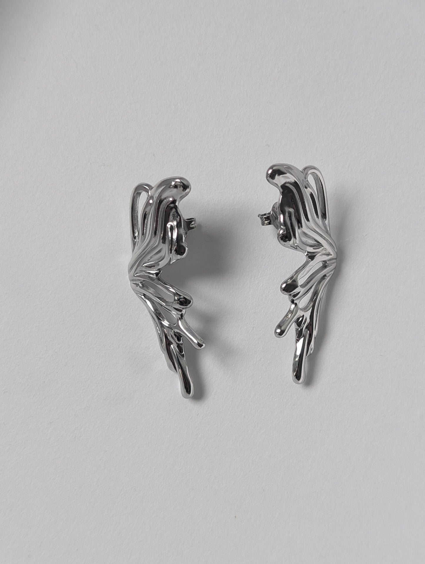 Flat‑lay of silver sculptural statement earrings front side up on white backdrop, waterproof PVD‑coated finish.