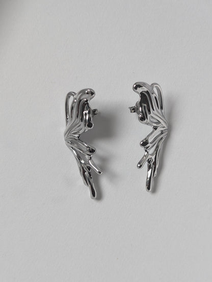 Flat‑lay of silver sculptural statement earrings front side up on white backdrop, waterproof PVD‑coated finish.