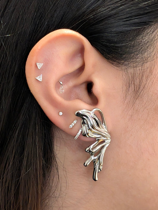 On‑ear close‑up of silver sculptural statement earrings—bold fluid design with tarnish‑resistant shine.