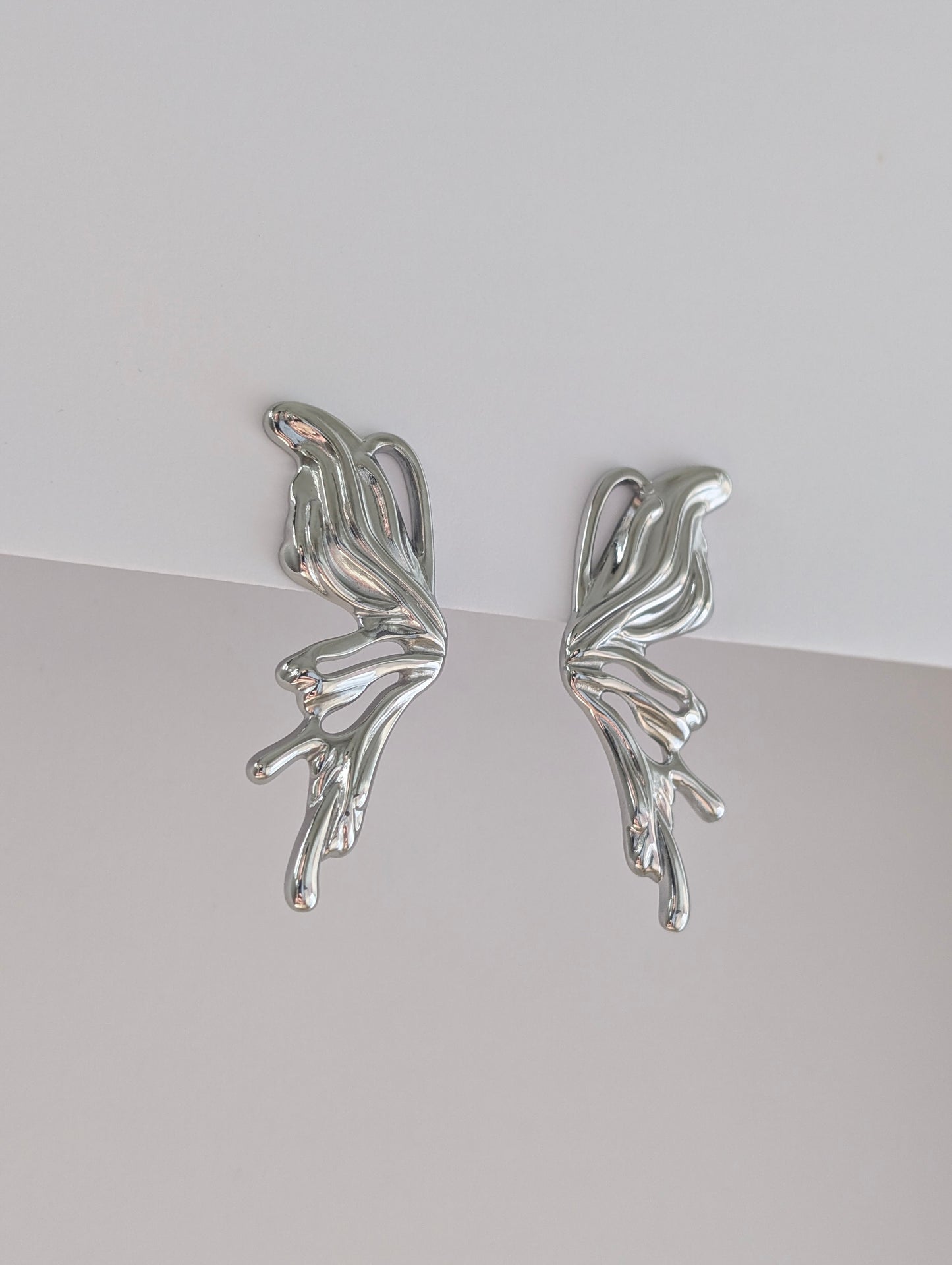 Second side view of silver sculptural statement earrings, fluid wave profile and polished stainless steel finish.