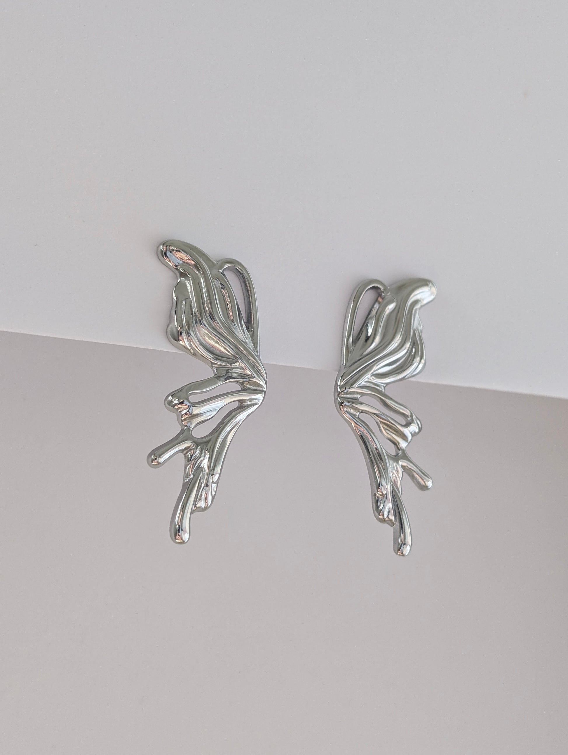 Second side view of silver sculptural statement earrings, fluid wave profile and polished stainless steel finish.