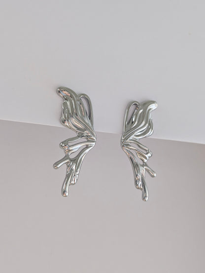 Second side view of silver sculptural statement earrings, fluid wave profile and polished stainless steel finish.