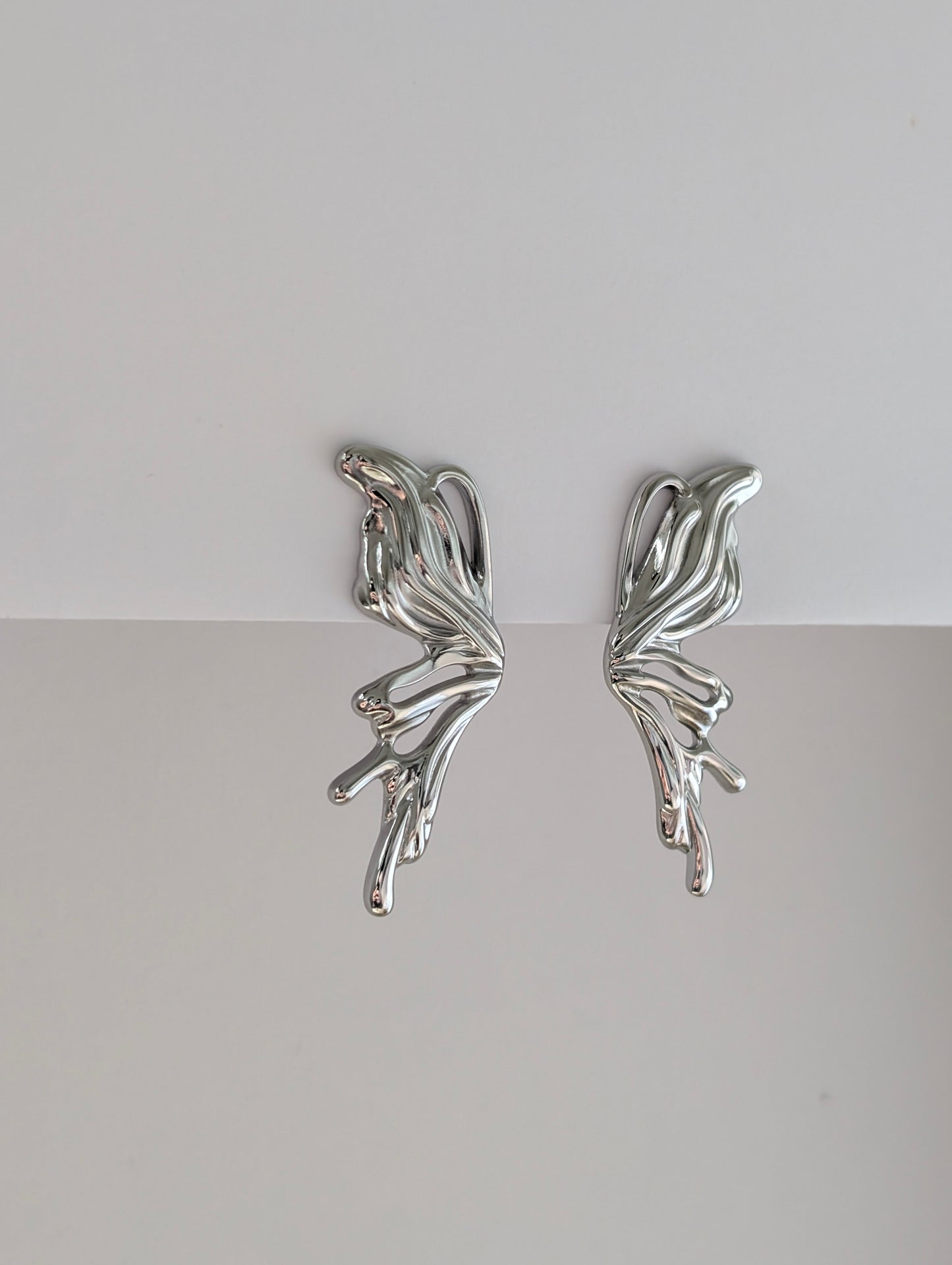 Side view highlighting fluid wave profile and hypoallergenic post of silver sculptural statement earrings.