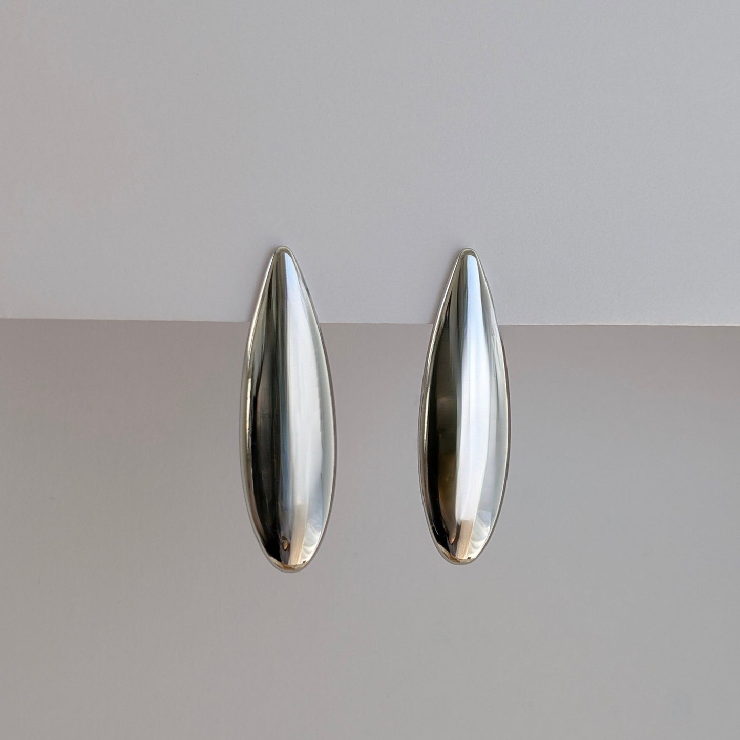 Side angle showing sleek teardrop profile and lightweight 10 g pair of silver statement earrings.