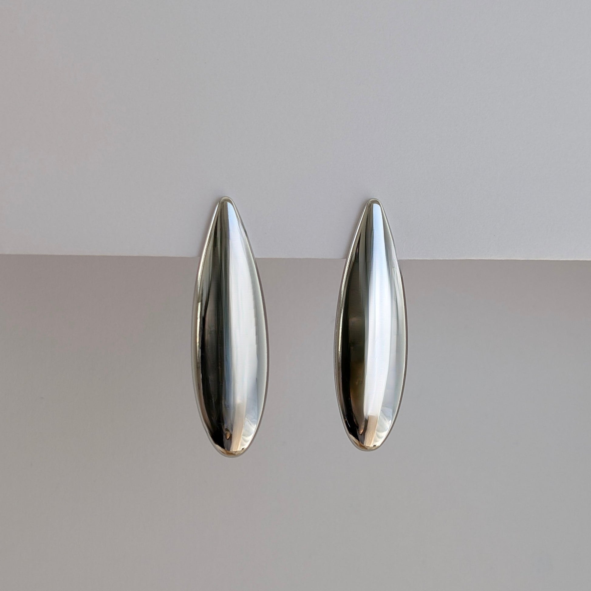 Side angle showing sleek teardrop profile and lightweight 10 g pair of silver statement earrings.